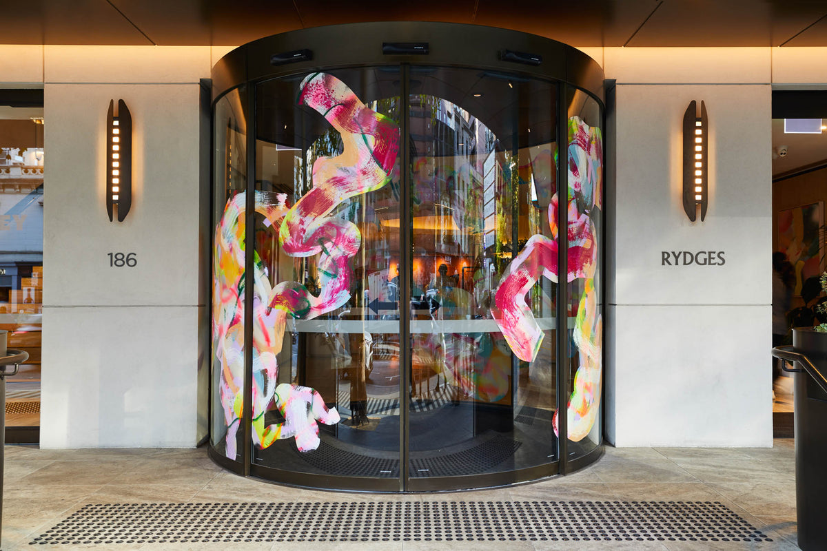 Decorative glass revolving door with colorful abstract artwork by Rowena Martinich at Rydges hotel entrance.