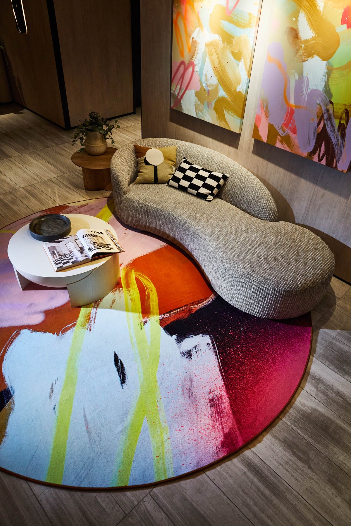 Modern living room with a curved gray sofa, colorful abstract carpet, and abstract art by Rowena Martinich on the wall.
