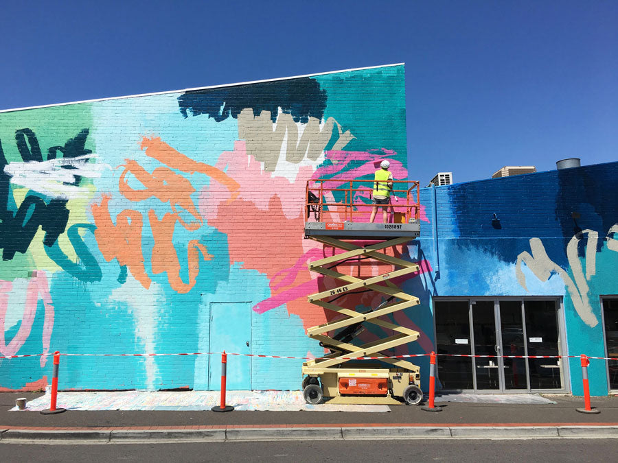 Rowena painting a mural in high-vis gear on a scissor lift.